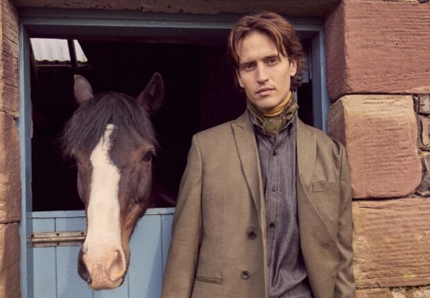 A man wearing a smart tailored suit stood next to a horse.